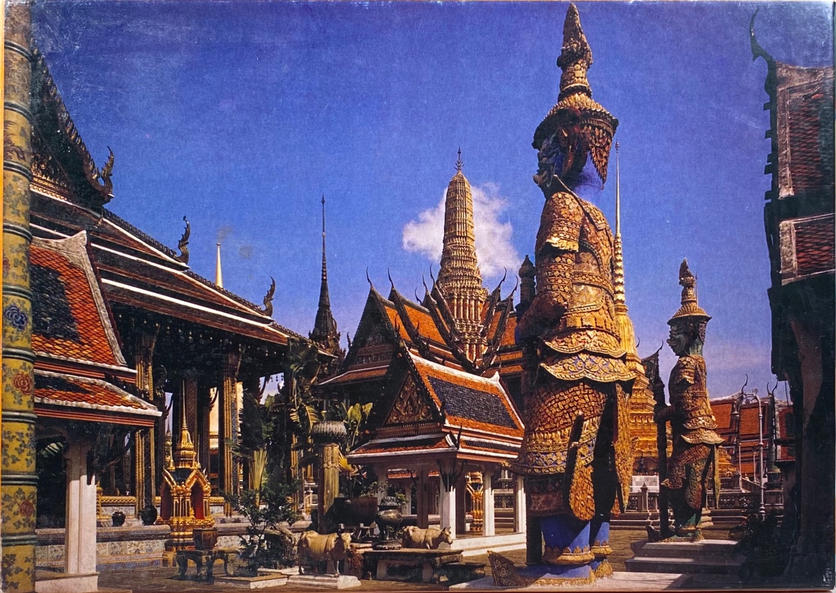 Two ornate guardian demon statues standing in the courtyard of a traditional Thai temple complex under a bright blue sky.