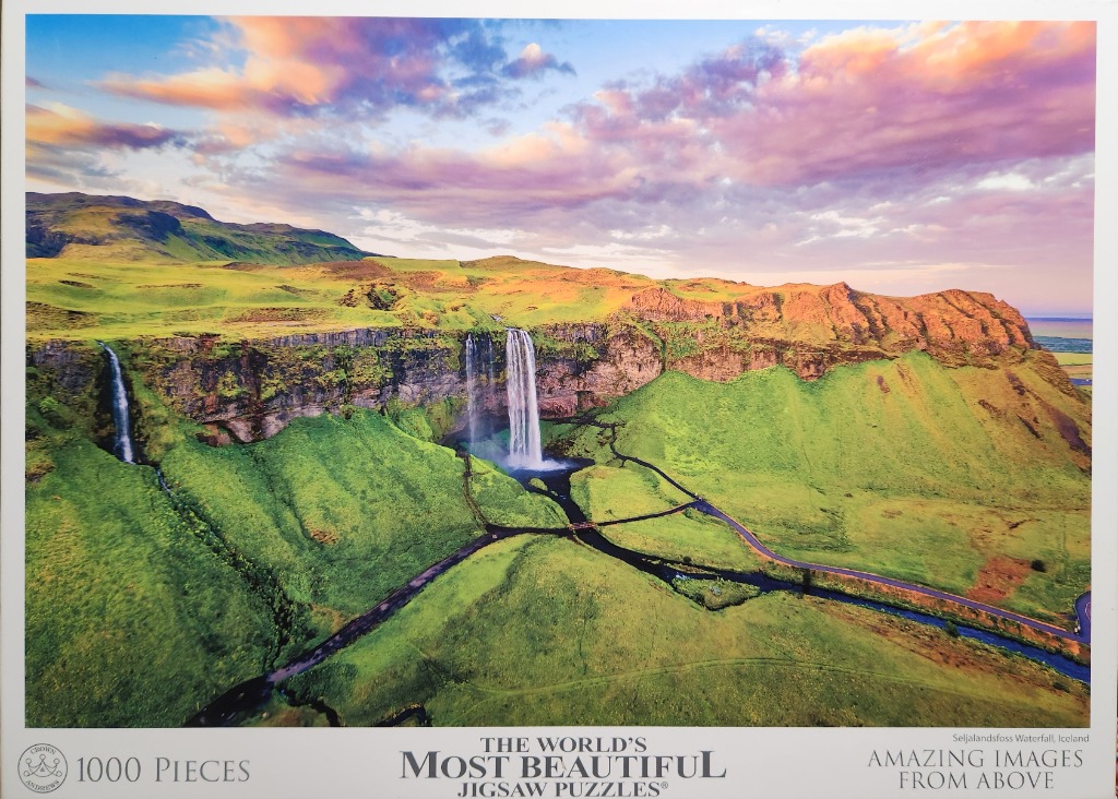 Aerial view of the Seljalandsfoss waterfall in Iceland during a sunset with green hills and dramatic clouds.