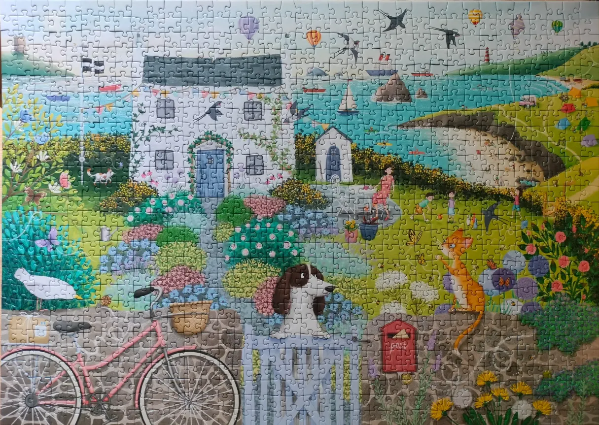 A whimsical seaside illustration of a white cottage with a garden, a bicycle, a spaniel, and a cat.