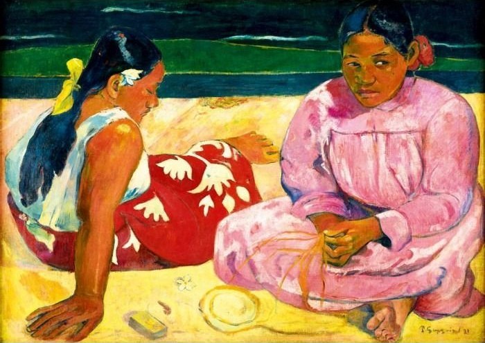 Two women with dark hair in colorful clothing sitting on a golden beach.