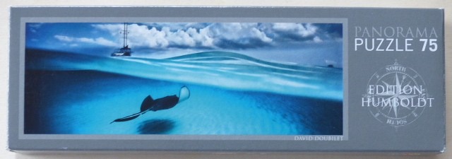 A split-level underwater photograph showing a stingray swimming below the surface and a sailboat in the distance.
