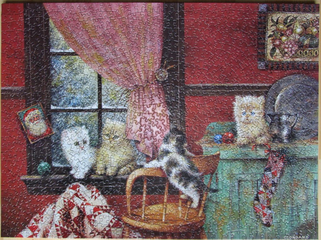 Three kittens sitting in a cozy, decorated room near a window with festive Christmas stockings and a quilt.