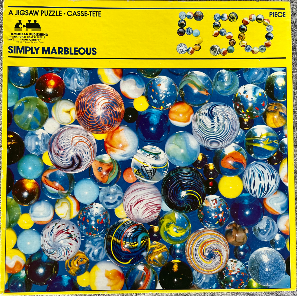 A collection of glass marbles of various patterns and sizes against a deep blue background.