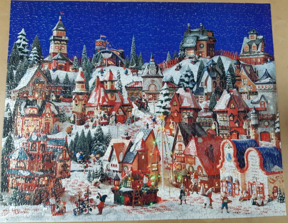 A festive Christmas village scene with colorful snow-covered buildings under a deep blue starry sky.