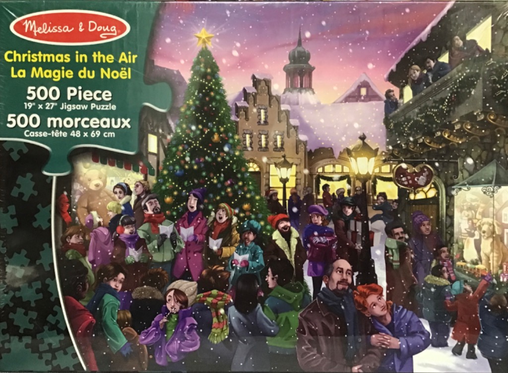 A group of people caroling around a large, decorated Christmas tree in a snowy village square at dusk.