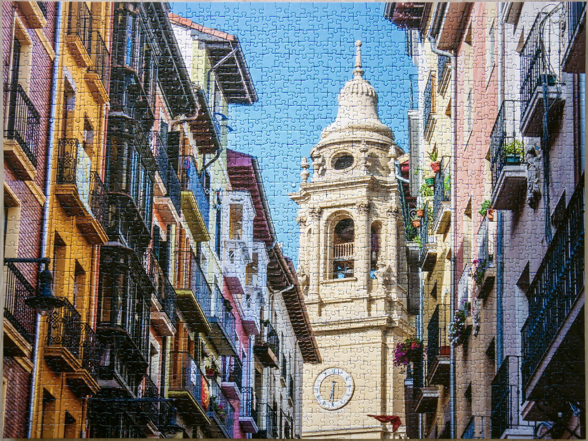 A narrow European street framed by colorful historic buildings leading to an ornate bell tower under a blue sky.