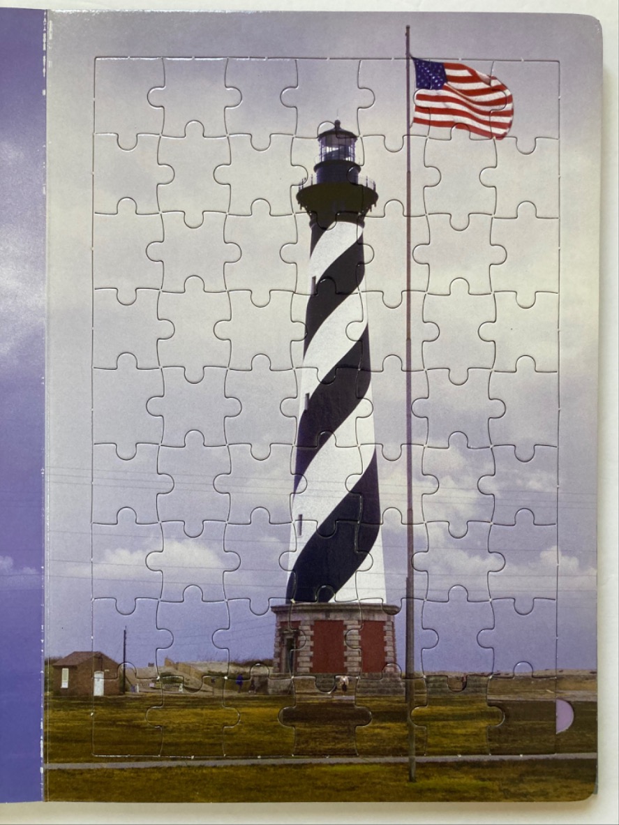 Cape Hatteras lighthouse with a waving American flag against a cloudy sky.