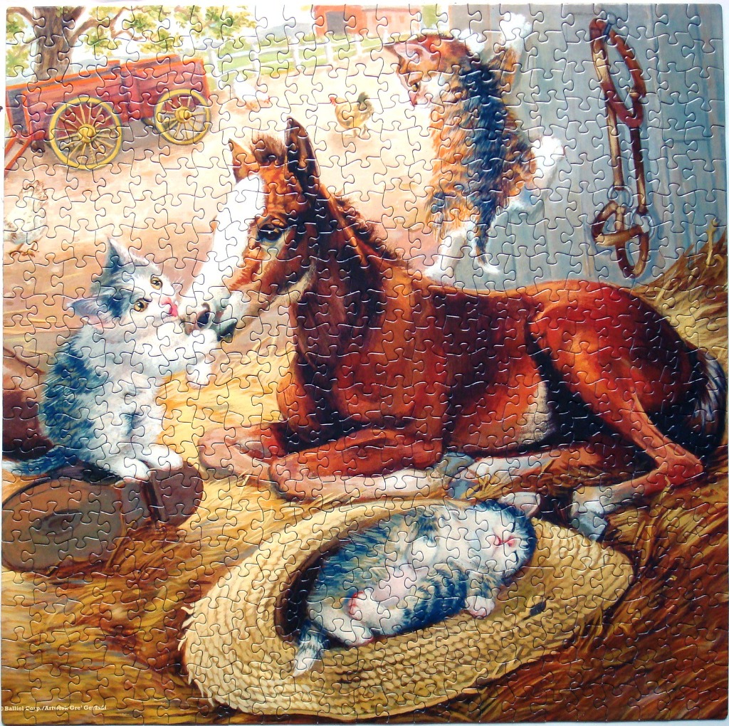 A horse lying in a barn with three kittens playing in the hay