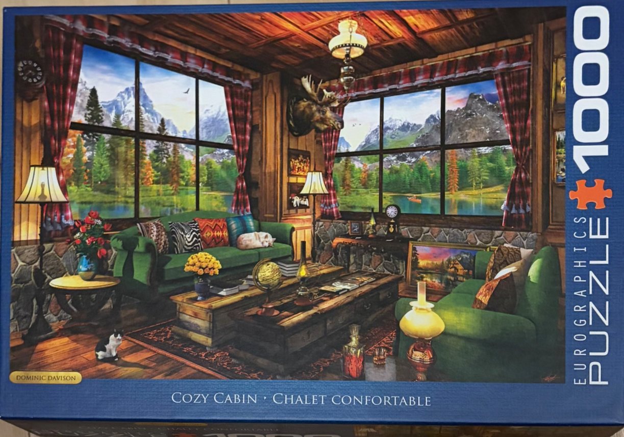 A cozy log cabin interior with two green sofas, a wooden coffee table, and a scenic view of mountains through large windows.