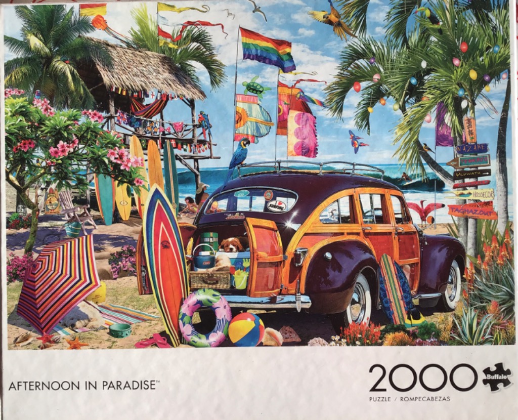 A vintage woody wagon packed with beach gear sits on a sandy shore under a bright blue sky filled with colorful flags.