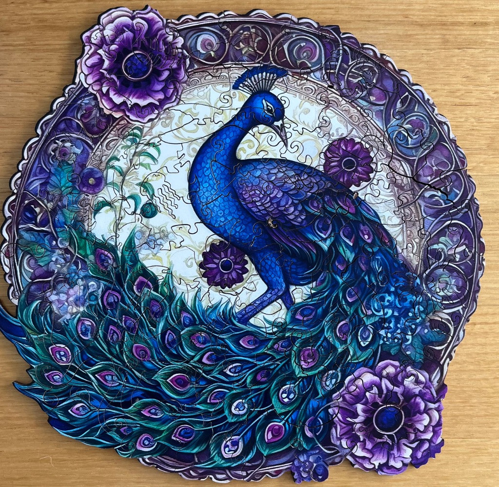 A circular illustration of a vibrant blue peacock surrounded by purple flowers and ornate, Art Nouveau-style framing.