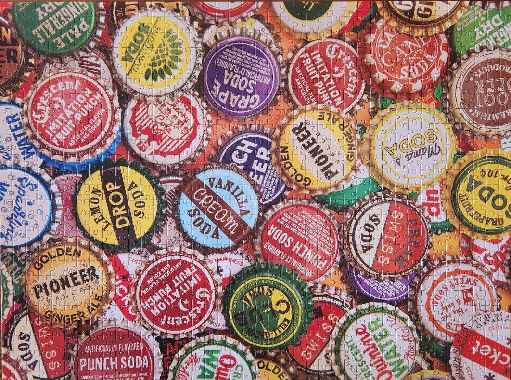 A dense, overhead collection of vintage metal soda bottle caps with colorful brand labels.