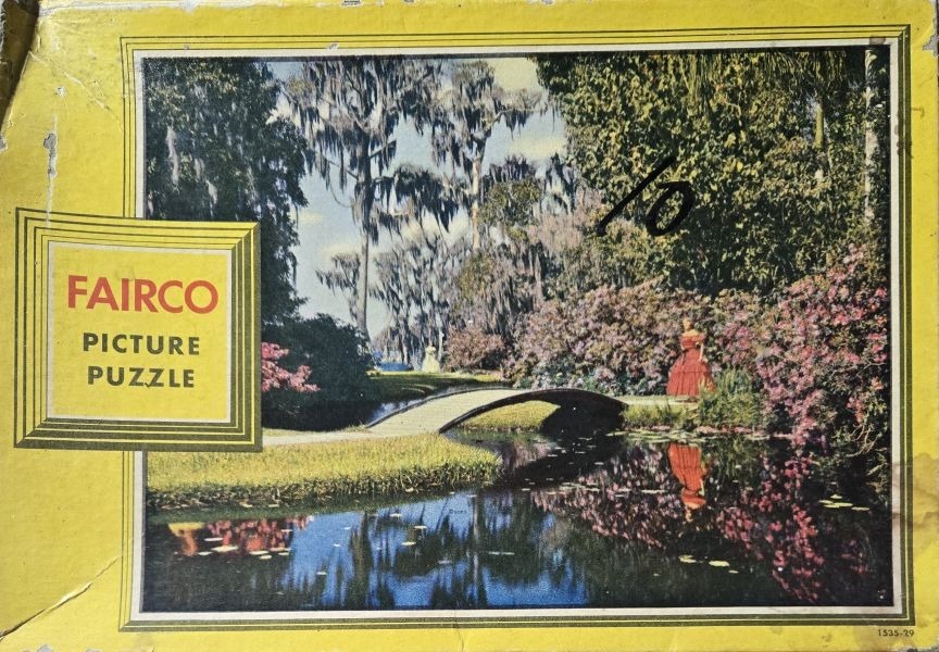 Vintage outdoor scene of a woman in a red dress standing by a pond with a stone bridge and Spanish moss trees.