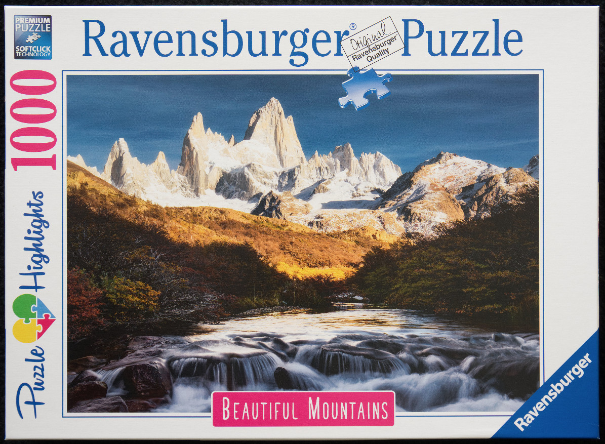 A scenic mountain landscape featuring snowy peaks, a golden hillside, and a rushing river in the foreground.