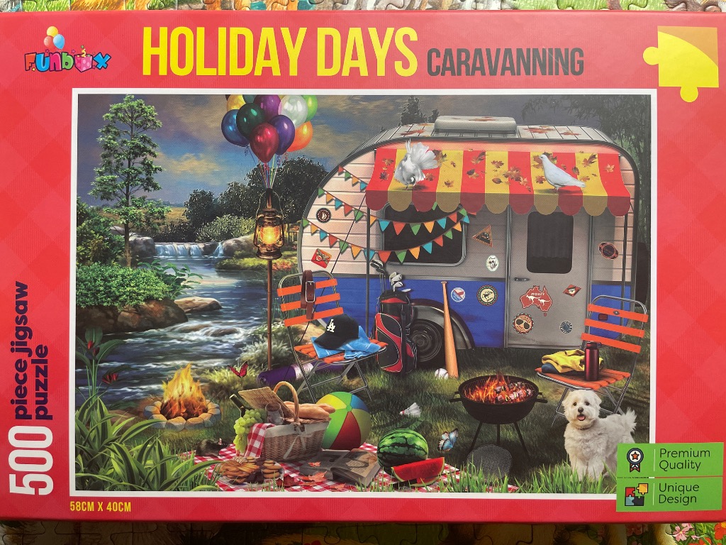 A vintage-style caravan parked by a stream with a campfire, picnic, and small white dog.