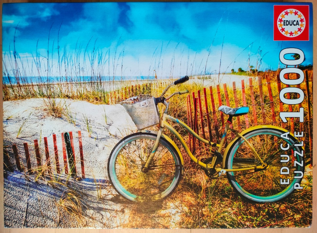 A yellow cruiser bicycle parked on a sandy beach path next to a wooden fence under a bright blue sky.