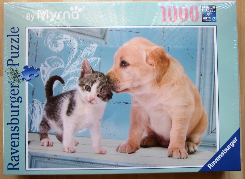 A golden retriever puppy nuzzling a small tabby and white kitten against a light blue background.