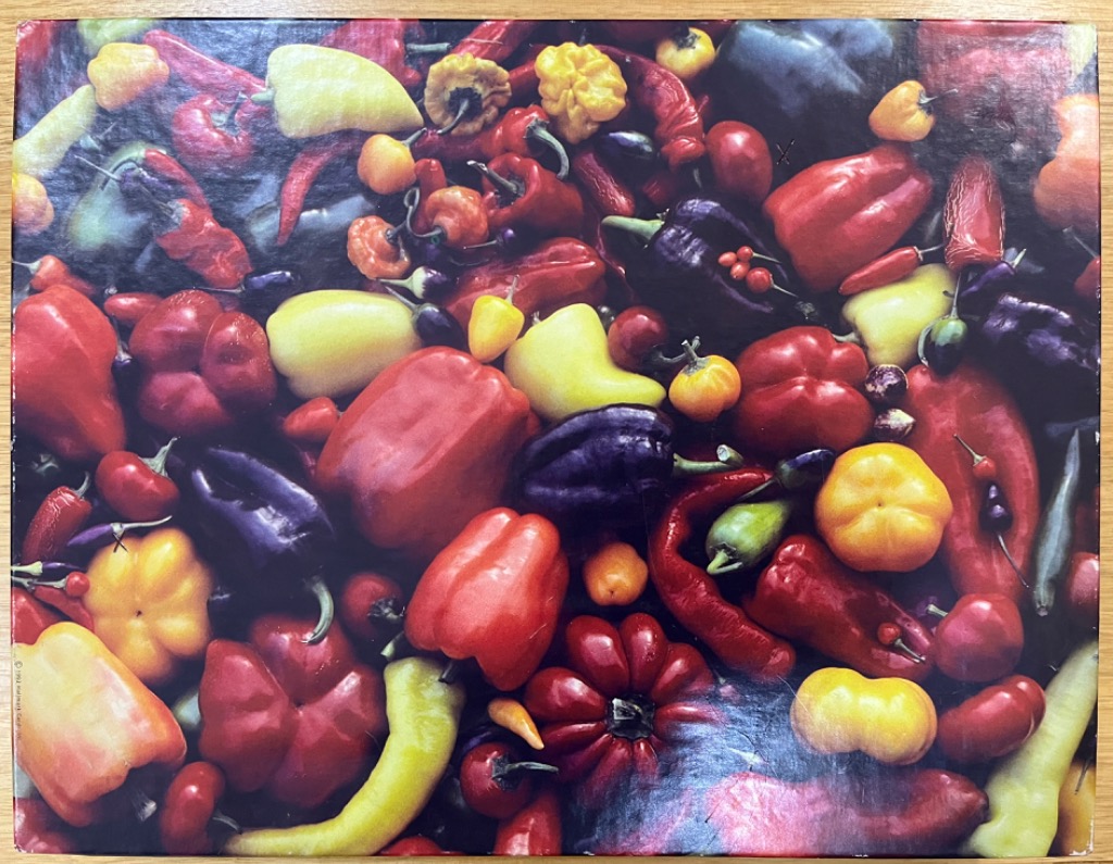 A dense, colorful collection of various chili and bell peppers in shades of red, yellow, and deep purple.