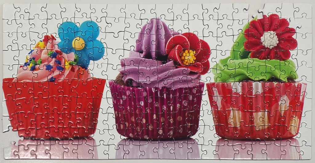 Three vibrant, decorated cupcakes in colorful wrappers arranged in a row against a white background.