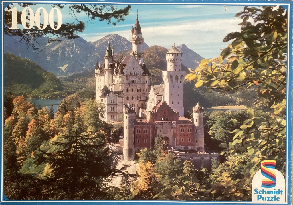Neuschwanstein Castle perched on a mountain ledge amidst an autumn forest under a blue sky.