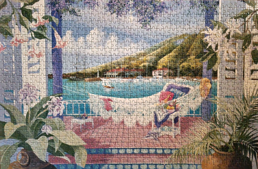 A serene terrace view overlooking a tropical harbor with a hammock, lush flowers, and a distant hillside.