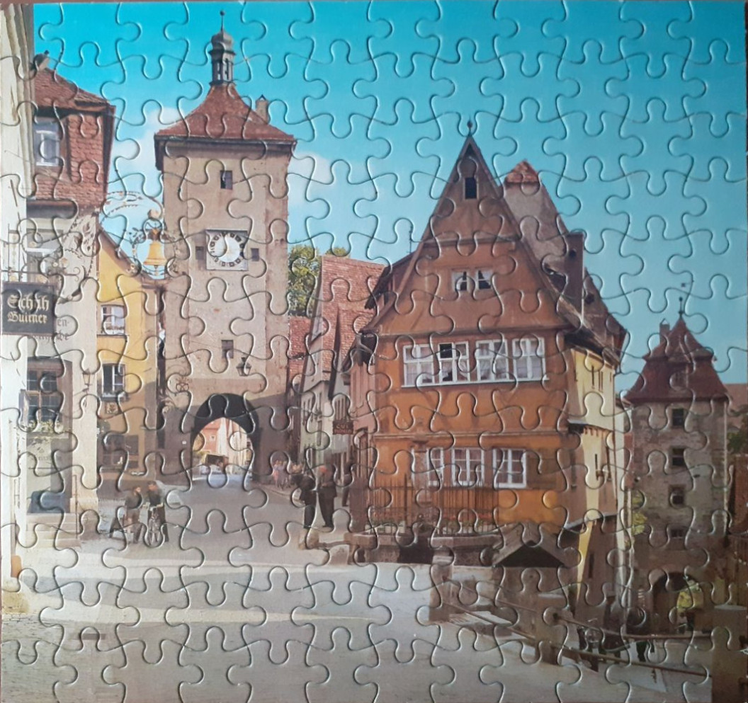 A sunny, historic European town square featuring half-timbered buildings and a stone clock tower.
