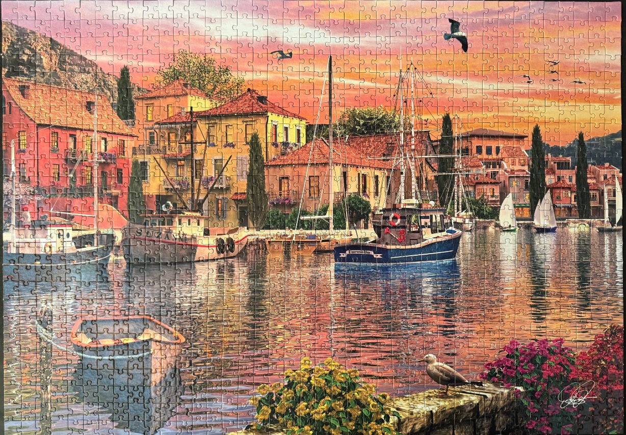 A Mediterranean harbor scene at sunset with colorful buildings, boats, and a stone embankment.