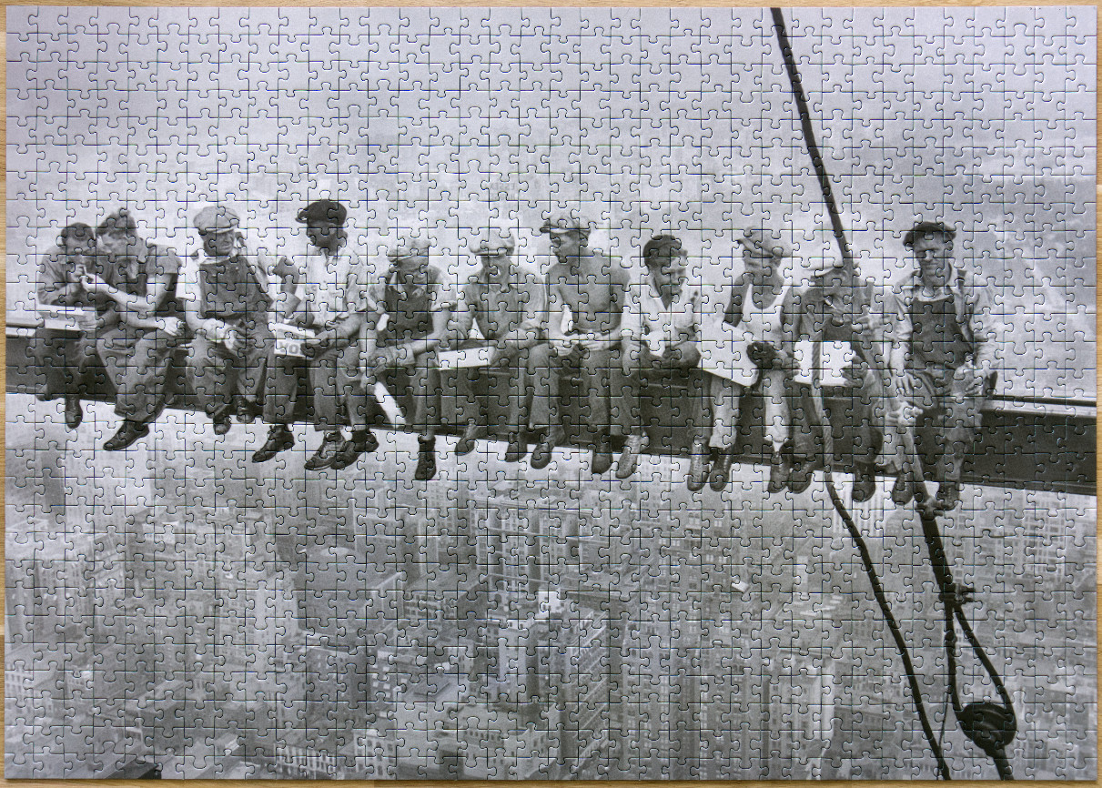 Black and white photograph of eleven construction workers eating lunch while seated on a steel beam above a city.