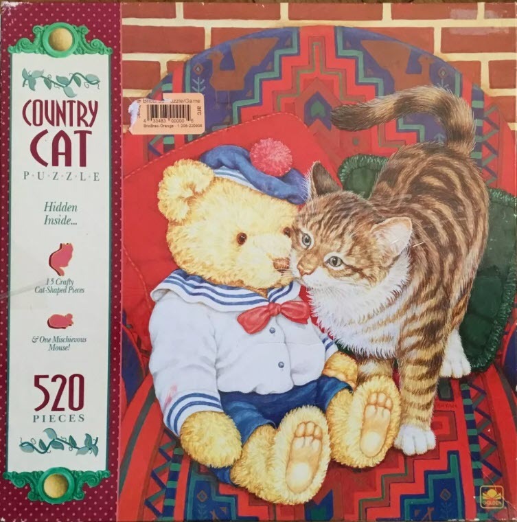A teddy bear dressed as a sailor sitting next to a brown tabby cat in front of a patterned backdrop.