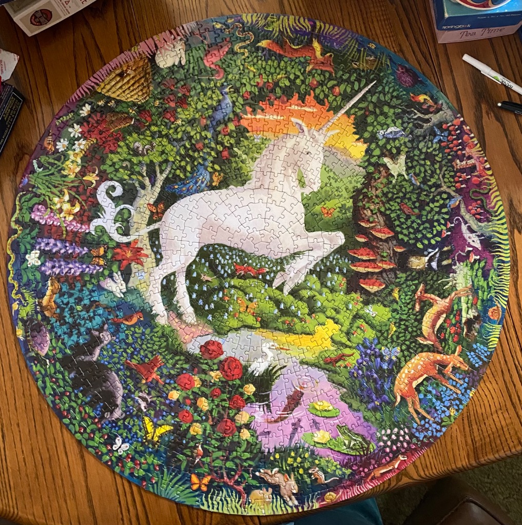 A circular illustration of a white unicorn standing in a lush, vibrant forest filled with flowers and wildlife.