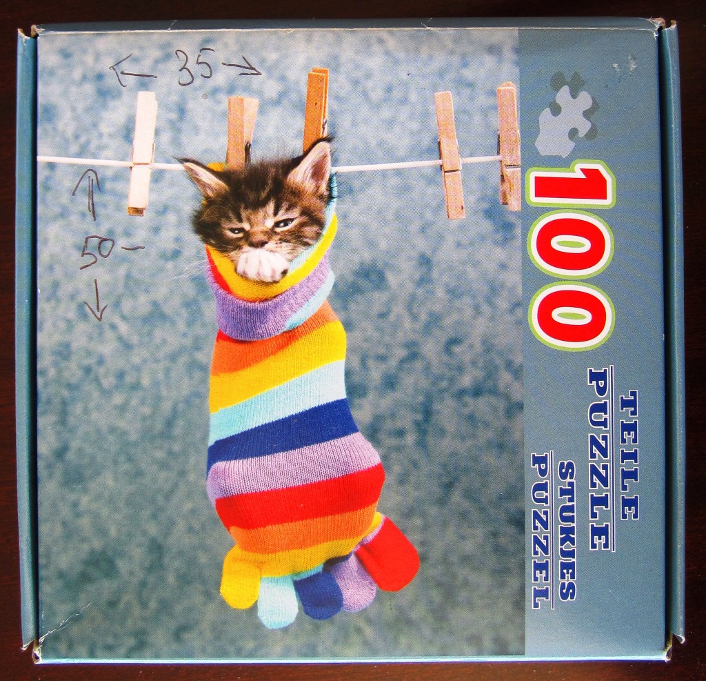 A cute brown tabby kitten snuggled inside a colorful striped toe sock hanging from a clothesline.