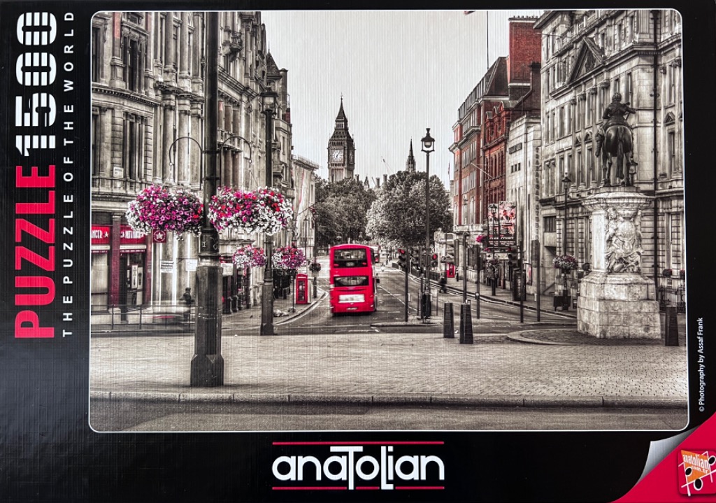 A black and white street scene of London with a vibrant red bus, red phone booths, and pink flower baskets.