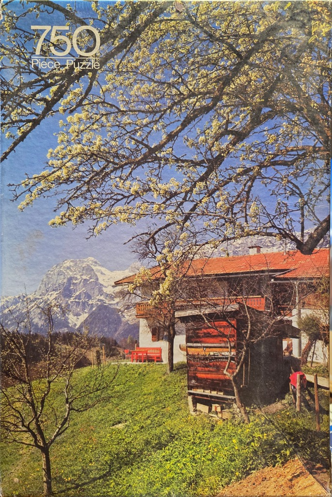 A sunny spring landscape featuring a rustic house, blooming trees, and snow-capped mountains in the background.