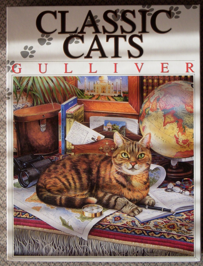 A tabby cat resting on a map-covered desk surrounded by travel-themed items like a globe, books, and binoculars.