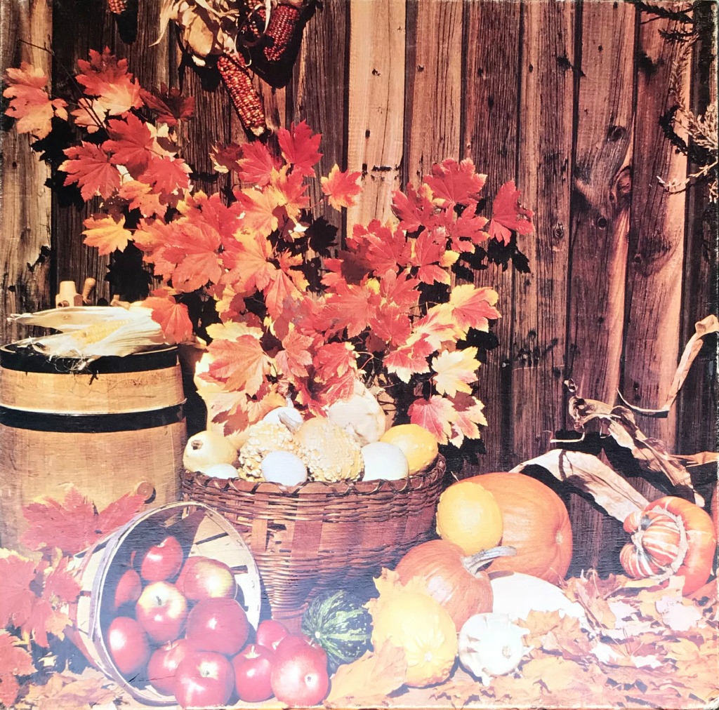 Autumn harvest display with apples, pumpkins, and maple leaves against a rustic wooden wall