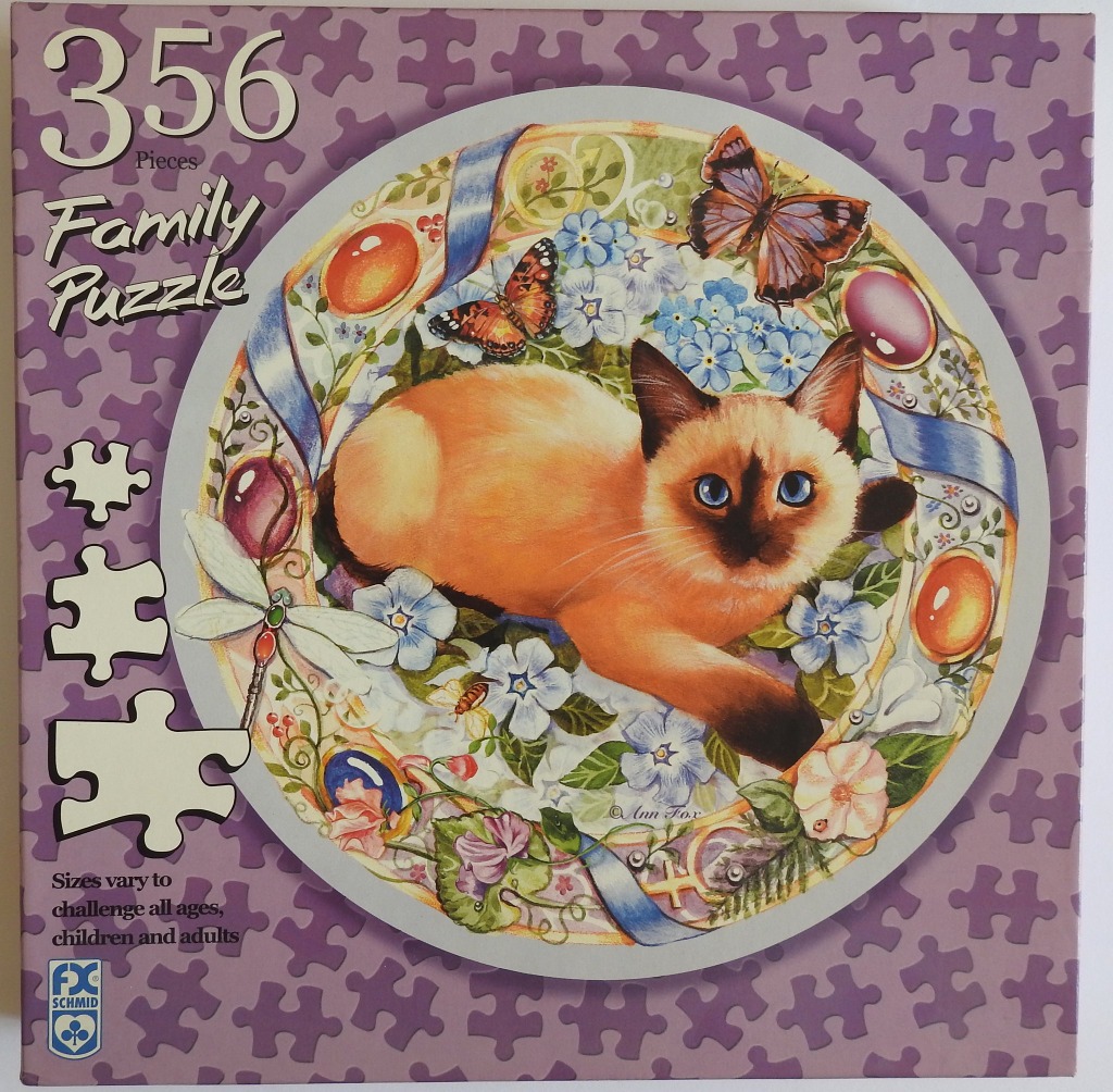 A Siamese cat resting among forget-me-not flowers, butterflies, and colorful cabochon jewels in a circular illustration.