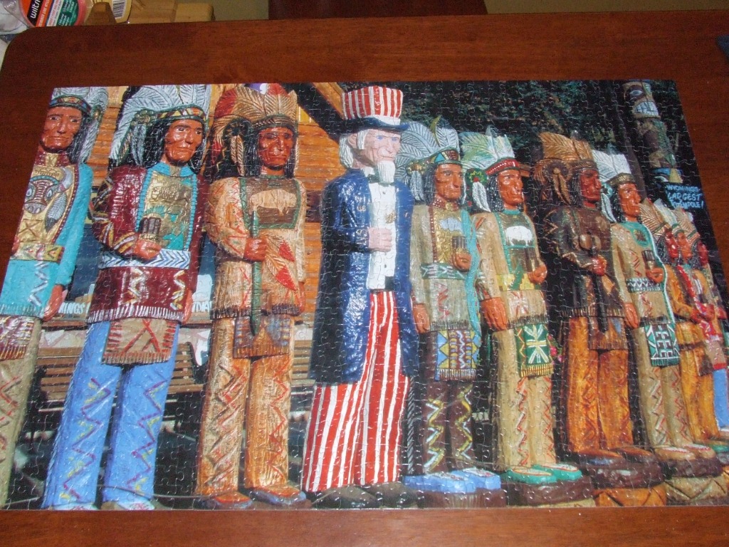 A row of hand-carved wooden statues featuring Native American figures and Uncle Sam standing outside a log building.