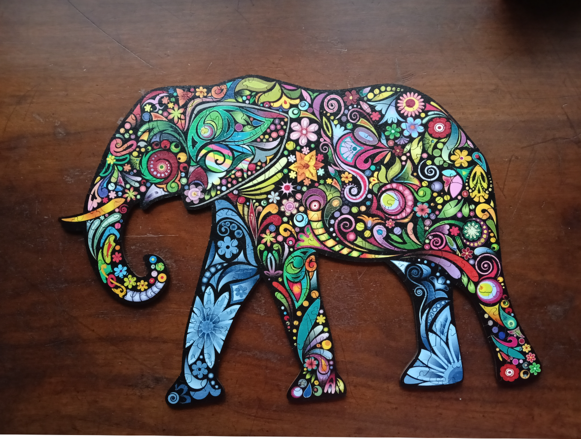 A decorative, silhouette-style elephant covered in colorful, intricate floral and paisley patterns against a wood background.