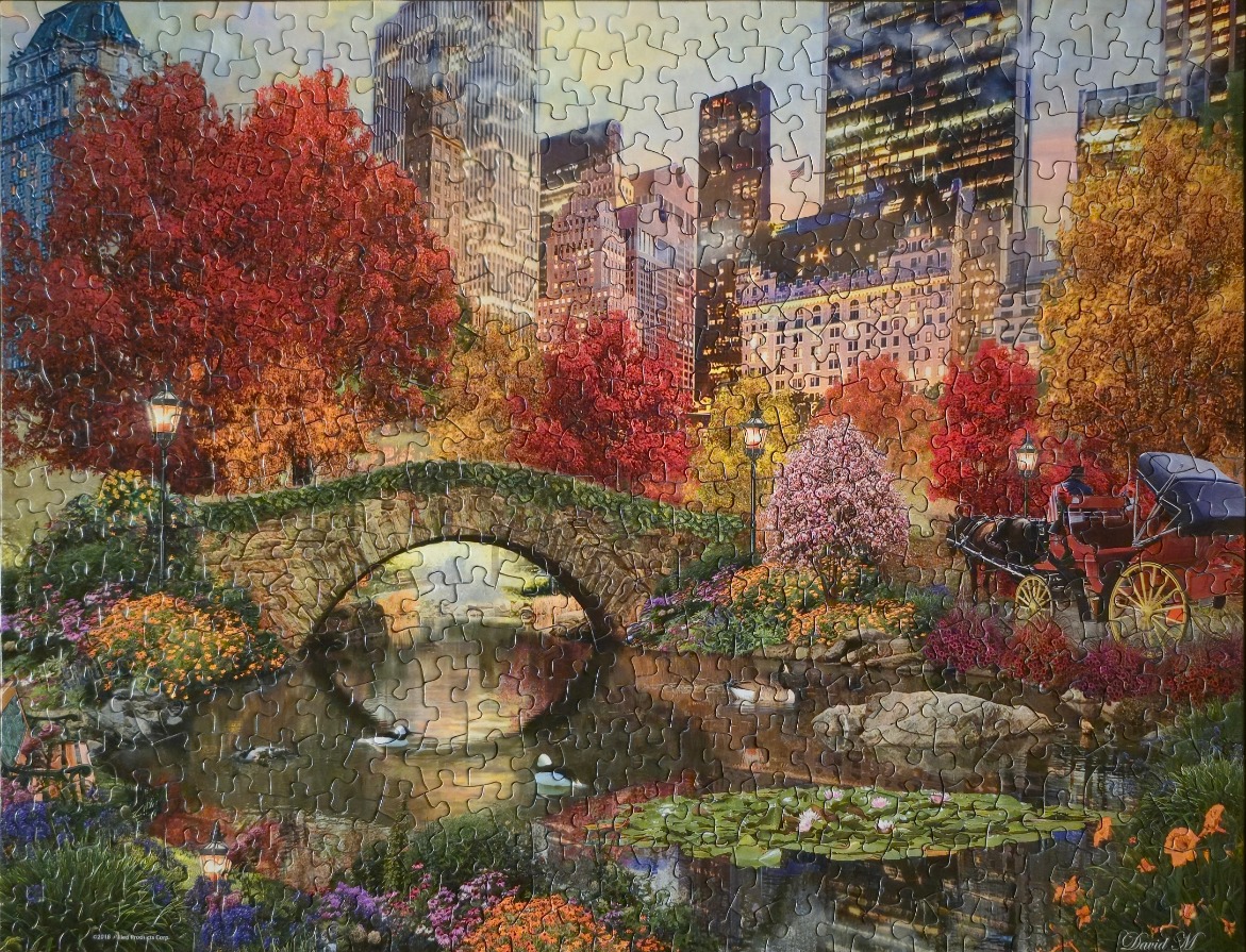 A scenic autumn view of a stone bridge and horse-drawn carriage in Central Park with a city skyline backdrop.