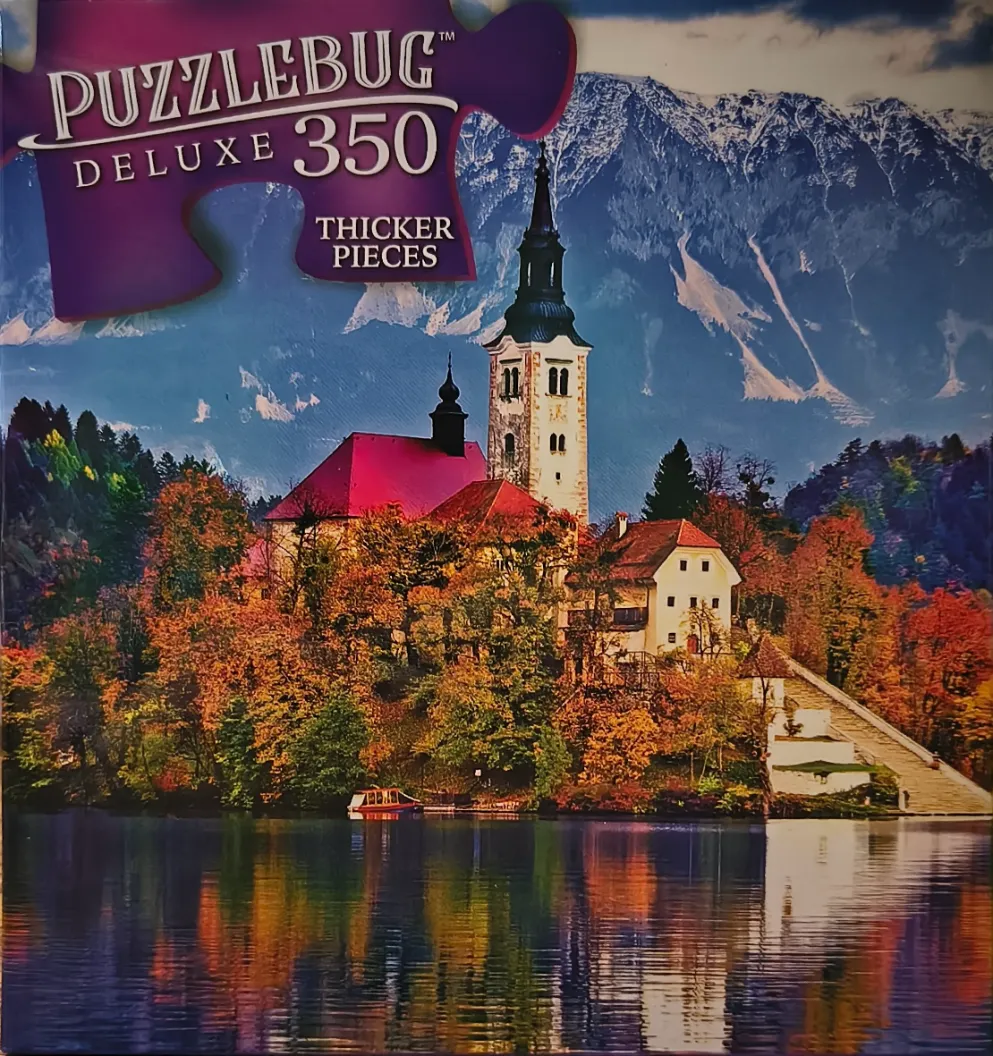 A church sits on an island in a lake surrounded by autumn trees with snow-capped mountains in the background.