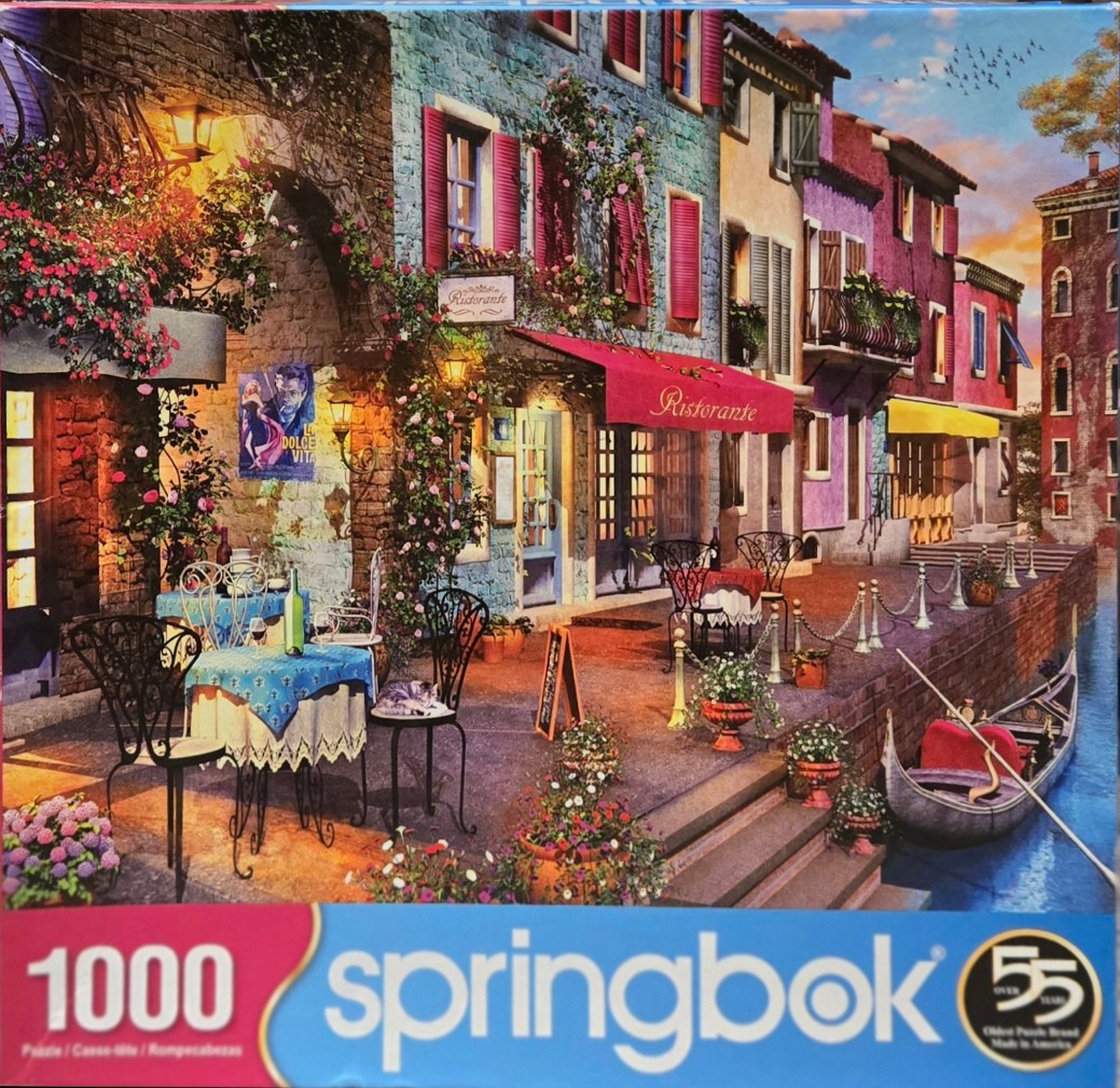 A scenic Italian-style canal-side restaurant with vibrant buildings and a gondola at sunset.