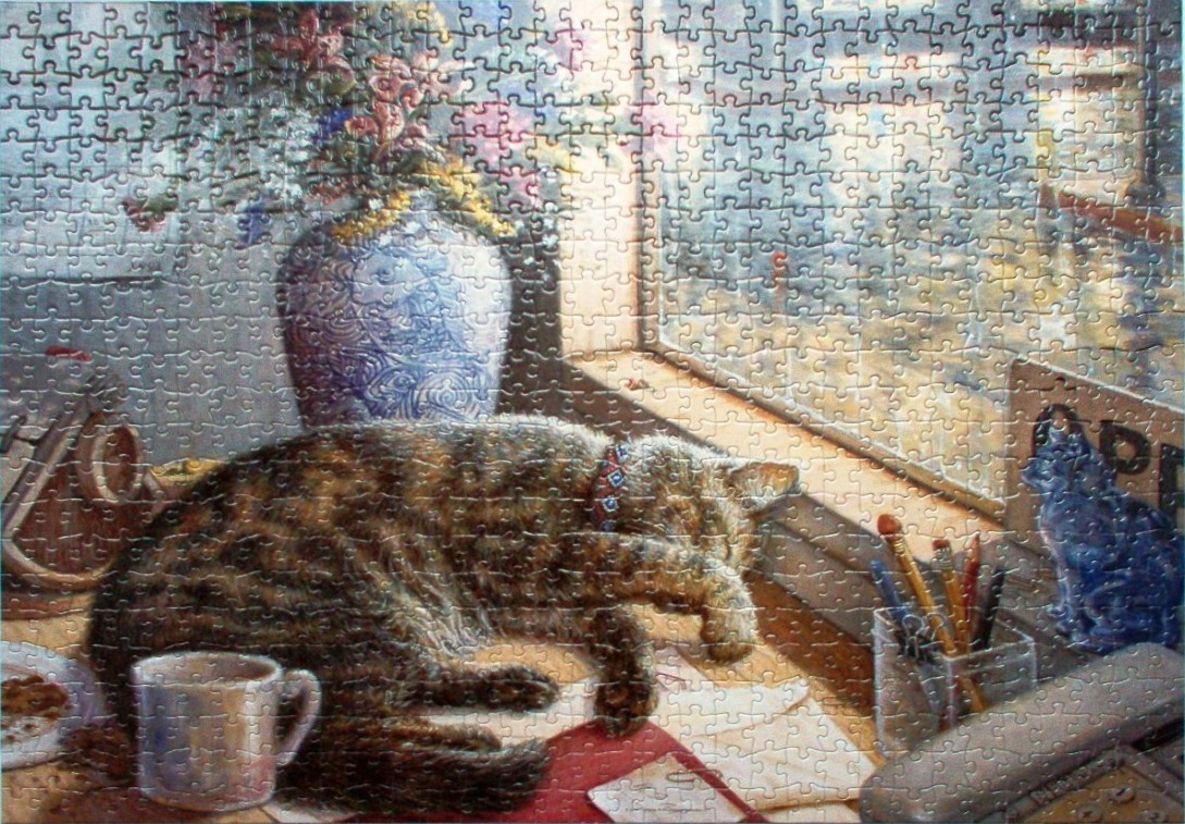 A tabby cat sleeping on a desk by a window with a vase of flowers and office supplies nearby.