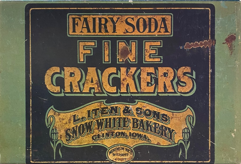 Vintage tin advertisement for Fairy Soda Fine Crackers featuring gold lettering on a black background.