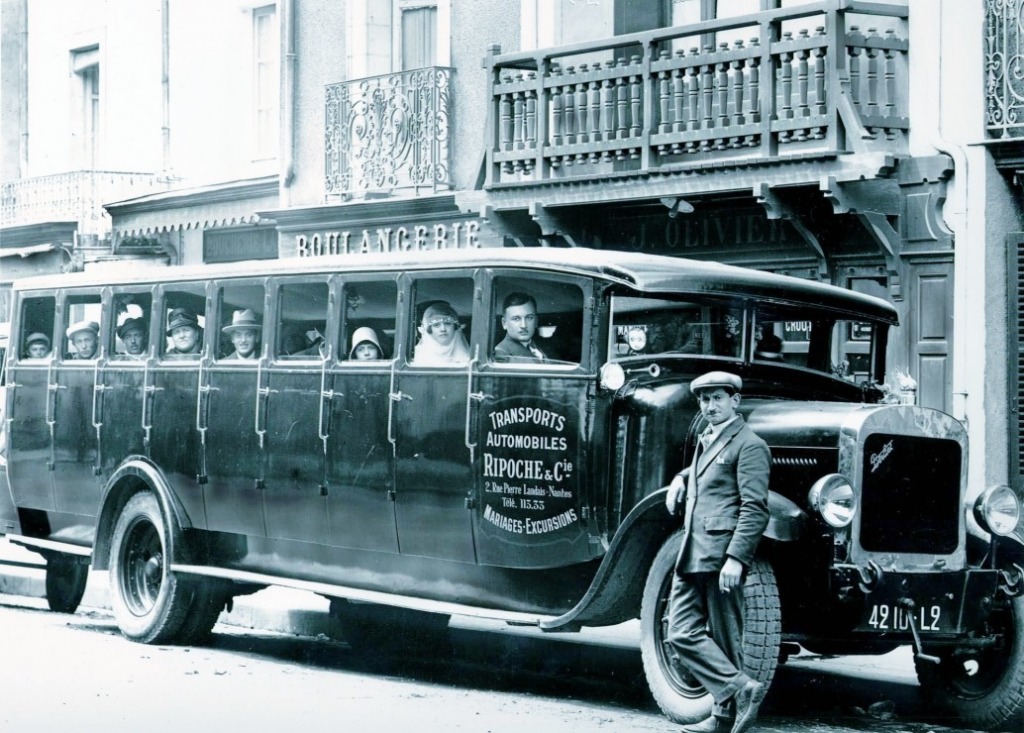 A black and white photograph of a vintage bus parked in front of a storefront with passengers visible inside.