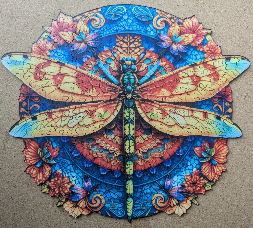 A circular art piece featuring a large, ornate dragonfly against a stained glass-style floral background.