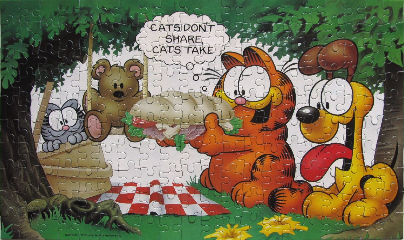 Garfield holding a sandwich while Odie looks on at a picnic in the woods.