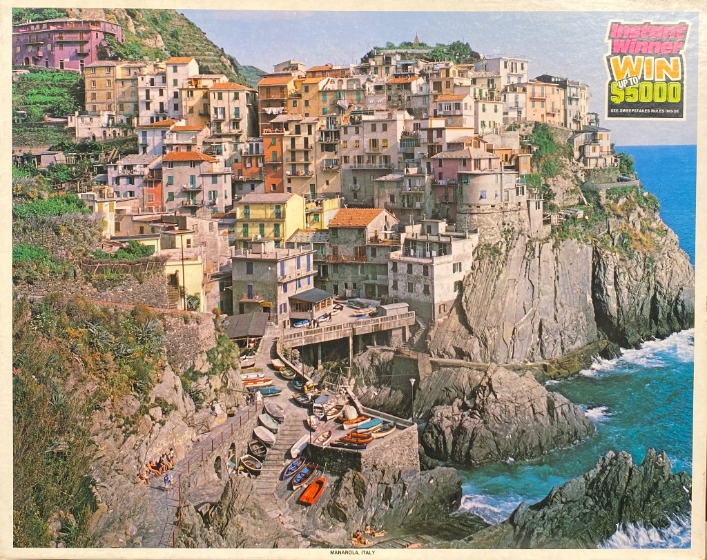 A sunny photograph of the colorful hillside village of Manarola, Italy, perched above the turquoise sea.