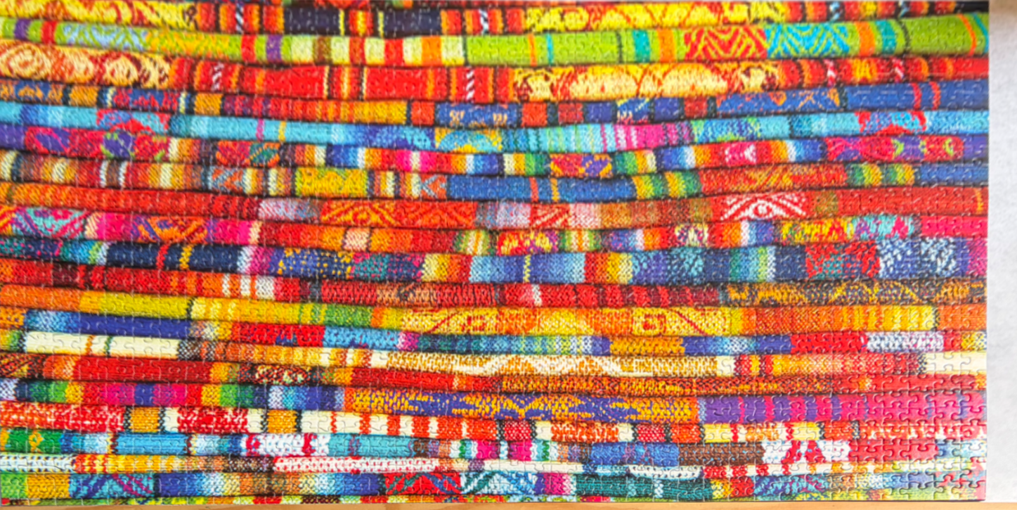 A close-up view of numerous tightly rolled, vibrant, patterned Andean-style textiles stacked horizontally.