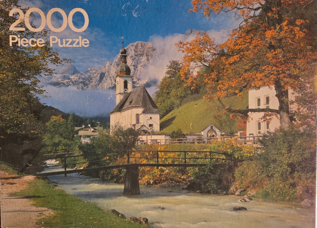 A scenic view of a Bavarian-style church by a mountain stream surrounded by autumn trees.
