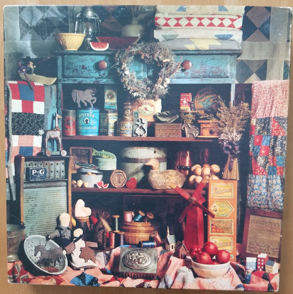 A still life featuring a rustic blue hutch filled with vintage Americana, quilts, and folk art items.